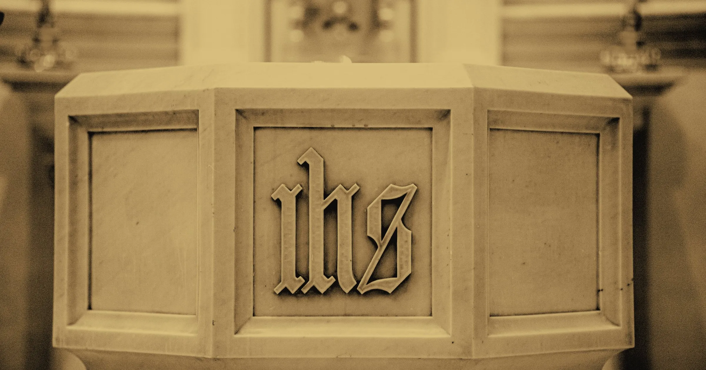 A stone baptismal font carved with the letters IHS