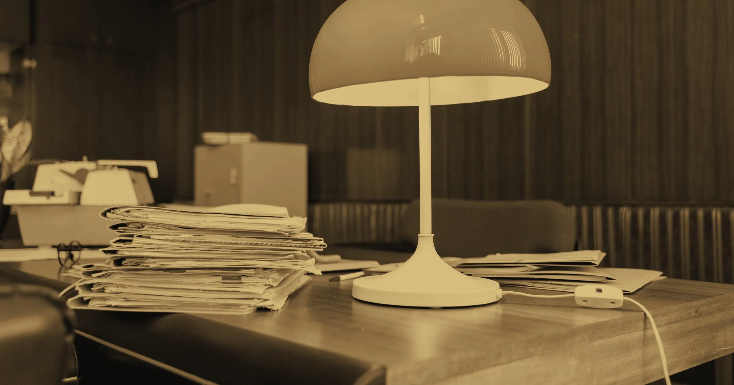 A desk stacked with documents beneath an old lamp