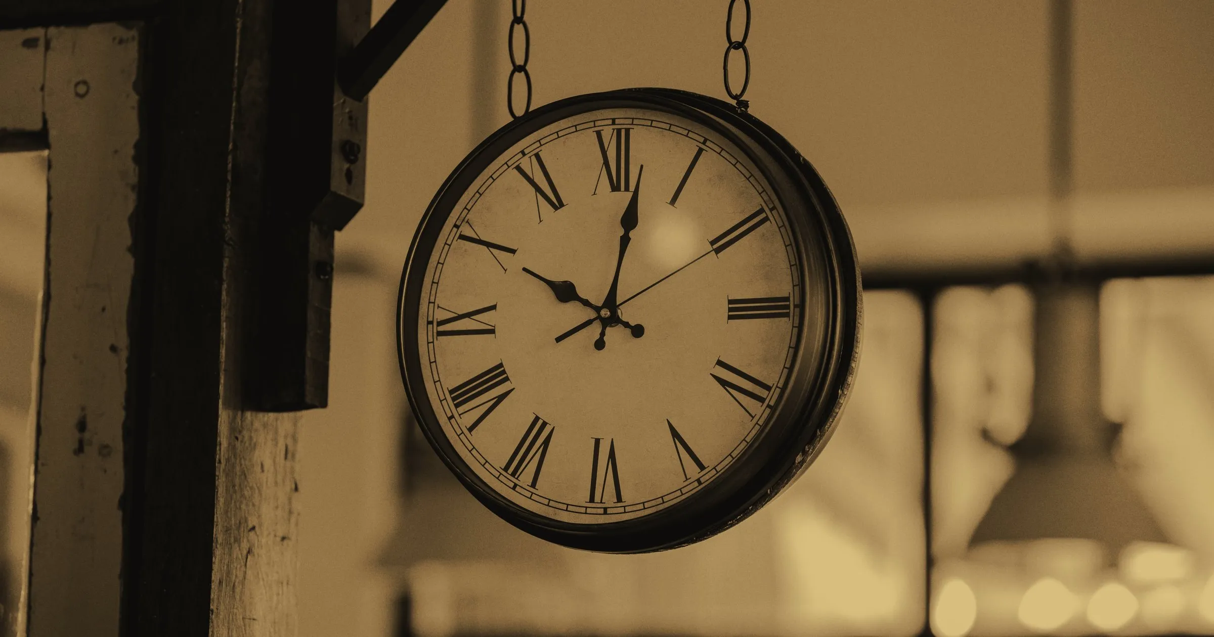An old station clock with Roman numerals hanging from chains