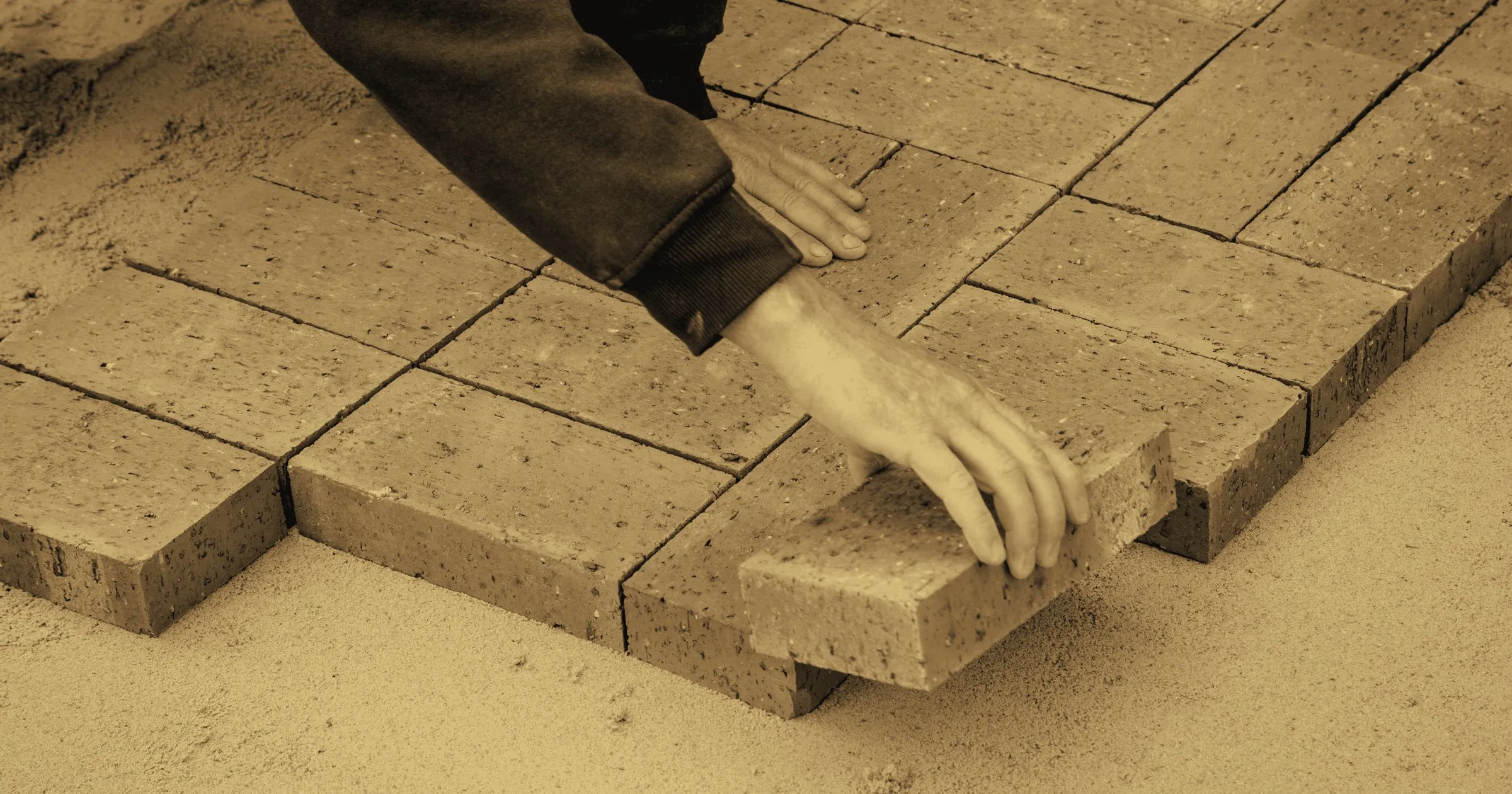 Hands laying bricks one by one on a sand bed