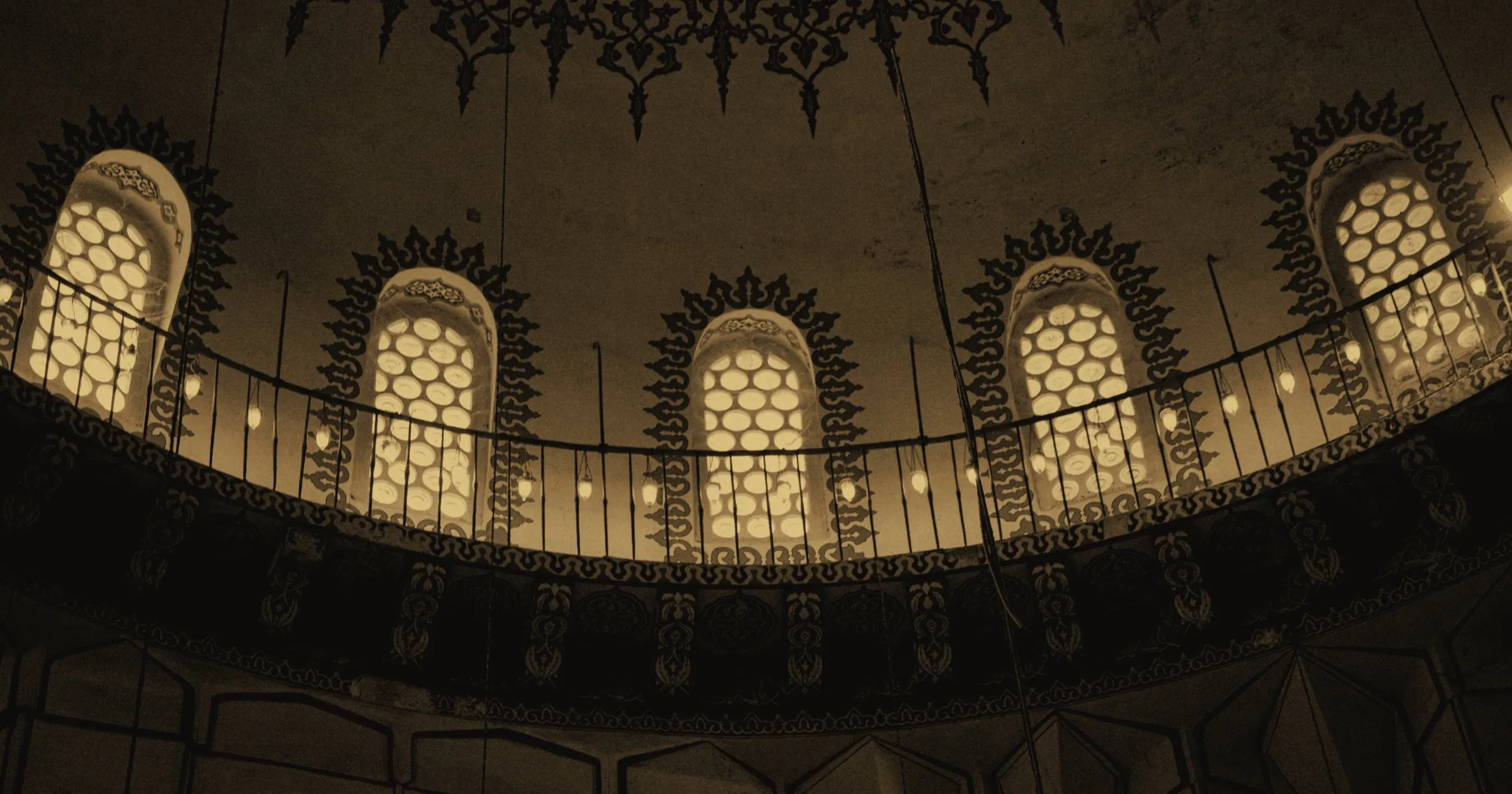 The upper gallery of a mosque, its arched windows lit from within