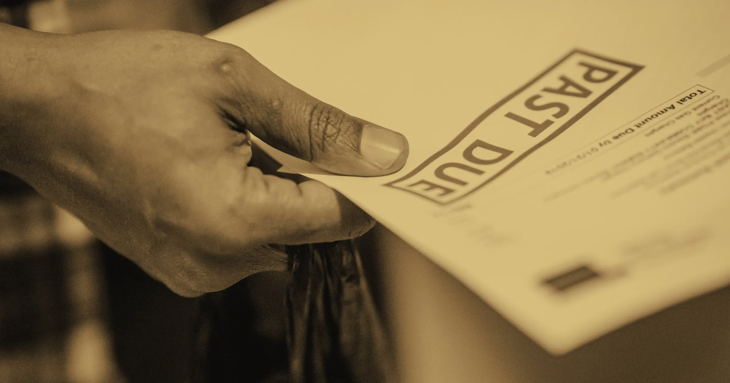 A hand holding a bill stamped 'Past Due'